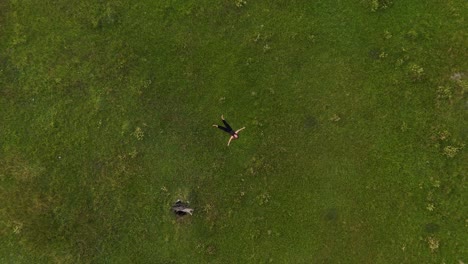 rising aerial top-down view of a serene young woman lying peacefully on open grassy land, gazing up at the sky.