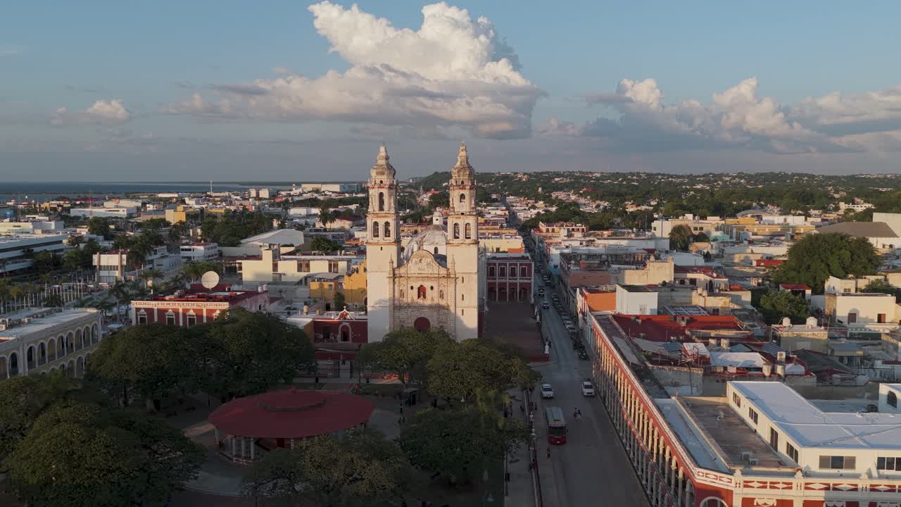 Side-moving drone shot of Campeche Cathedral, main square, and surrounding colonial streets bathed in golden light