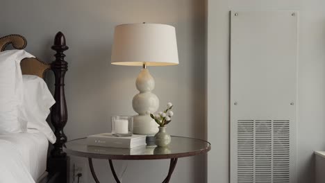 panning shot of a bed side glass table with white decorations including a white lamp