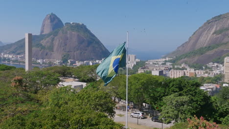 slow motion footage of the flag of brazil waving in the breeze with sugarloaf mountain in the background