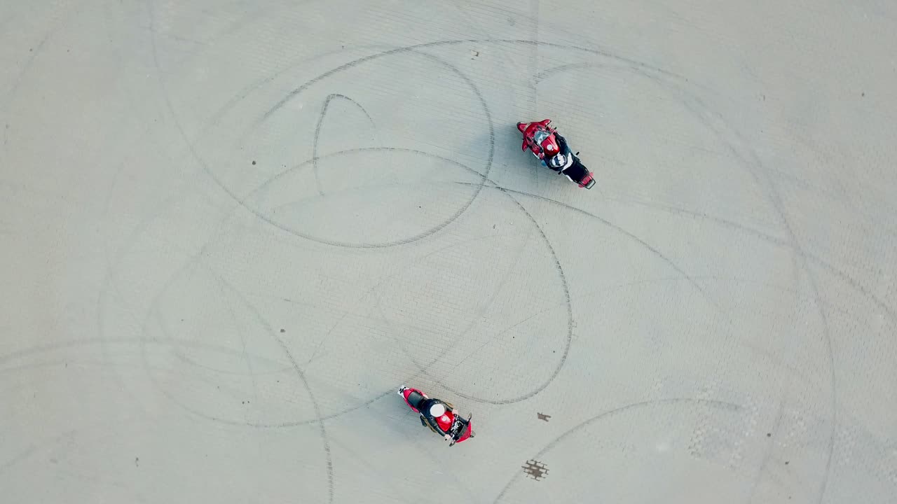 Top view of two professional motobikers racing highspeed on a road in a circle way. Bikers on their motorcycles training riding outdoors. Aerial view.