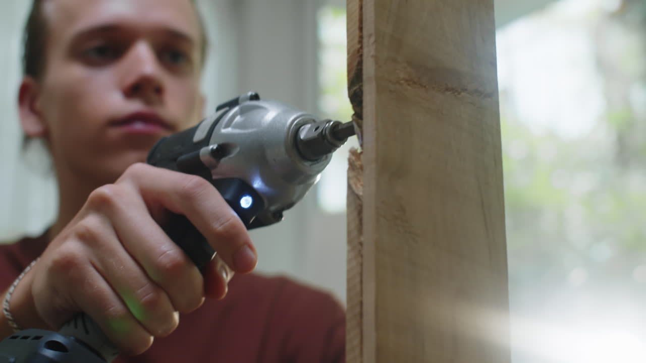 Young Guy Using Drill on Wooden Plank