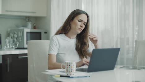 Sad-woman-working-laptop-at-white-kitchen.-Unhappy-person-use-computer