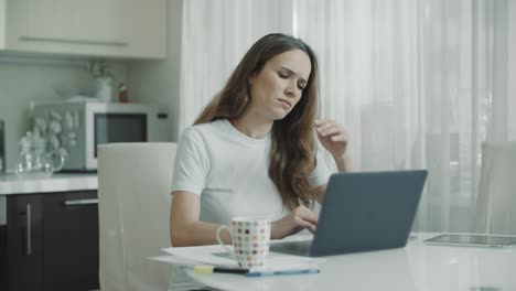 mujer triste trabajando con una computadora portátil en la cocina blanca. persona infeliz usar computadora