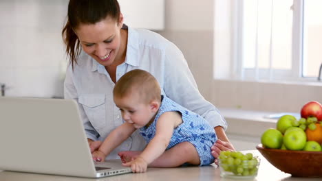 madre bonita usando la computadora portátil y jugando con el bebé