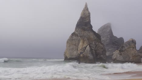 aggressive waves at praia da ursa, portugal with an imposing, tall rock nearby