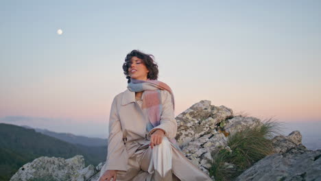 relaxed brunette sitting evening rocks enjoying serene ambiance. woman relaxing
