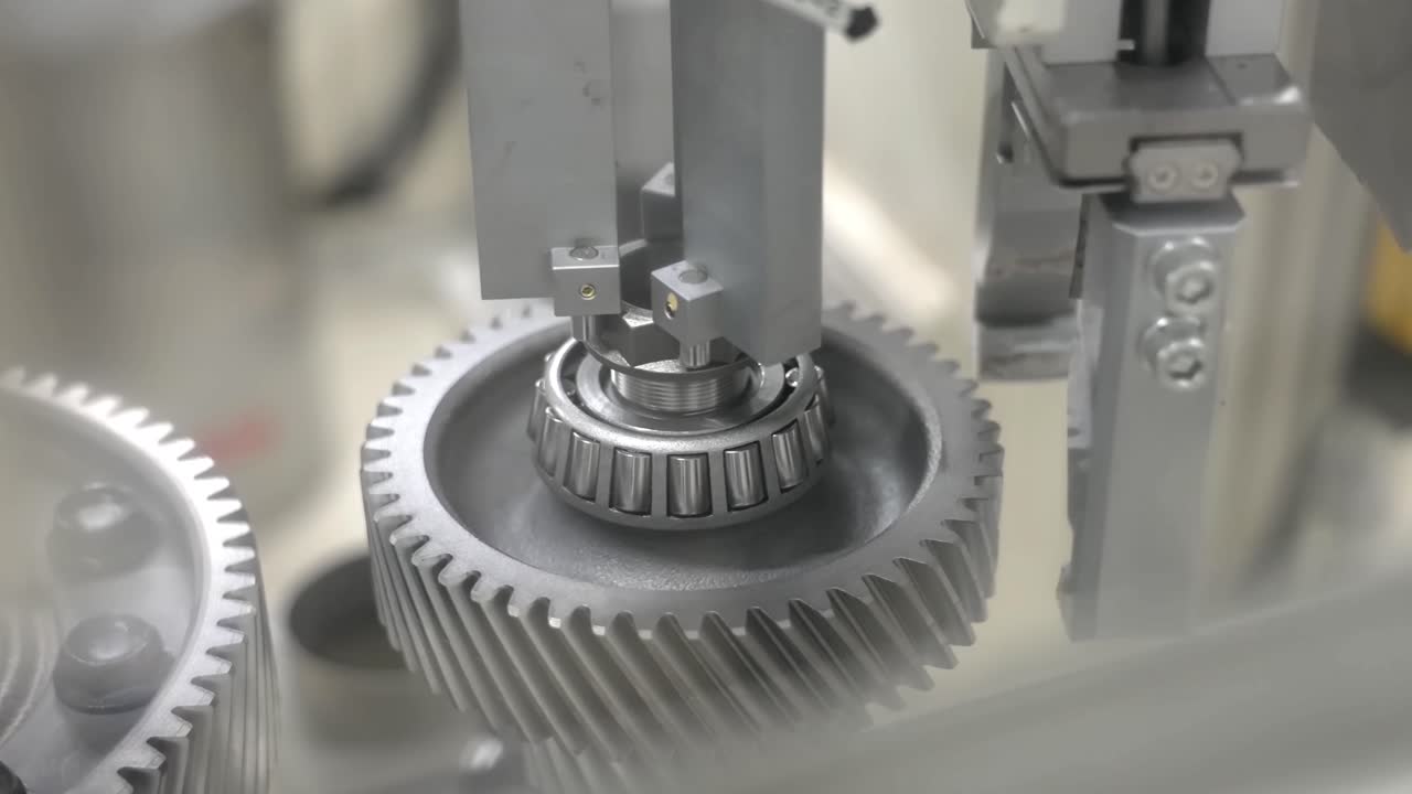 Close-up of an automated robotic gripper precision-tightening a hex nut onto a tapered roller bearing and helical gear assembly in a modern factory
