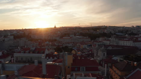 Drone-flying-around-historic-city-center.-Silhouette-of-buildings-against-setting-sun.-Evening-aerial-view.-Lisbon,-capital-of-Portugal.