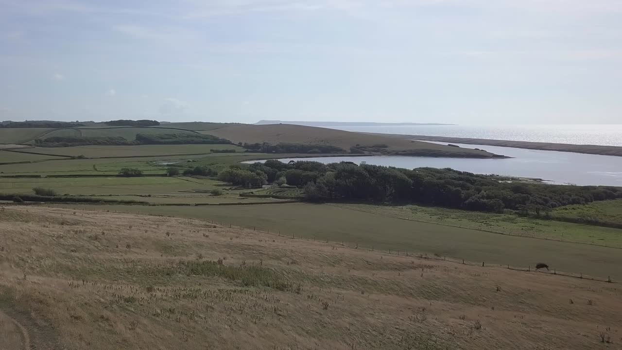 Låg, framåtföljande flygbild nerför en kulle mot Fleetlagunen vid den västra änden av Chesil Beach.