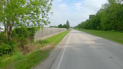 rear window point of view while driving down a road on the edge of midwestern town past a few homes, fences and fields