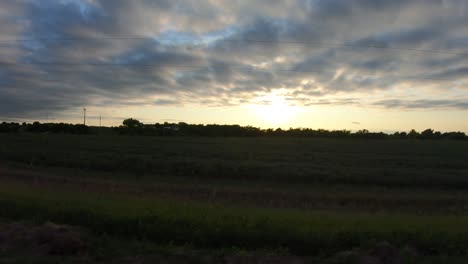 conduciendo a través de la zona rural de nebraska viendo una colorida puesta de sol con campos de maíz, postes de energía y un camino de grava visible