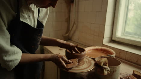 Young-ceramist-making-line-on-clay-product-in-studio.-Lady-working-with-wet-clay