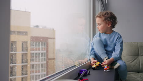 adoption-of-children-and-parenting-little-boy-is-sitting-alone-in-room-and-looking-on-falling-snow-through-window