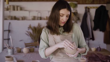 beautiful craftswoman making a clay bowl in a pottery workshop. she looks at the product and smiles. the concept of favorite hobby and creative development