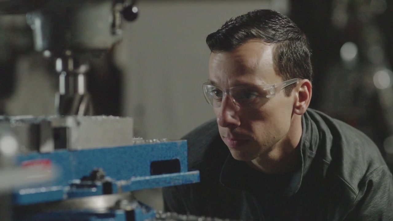 A close up slow motion shot of a mechanic inspecting a giant drill with safety glasses on in his mechanic shop