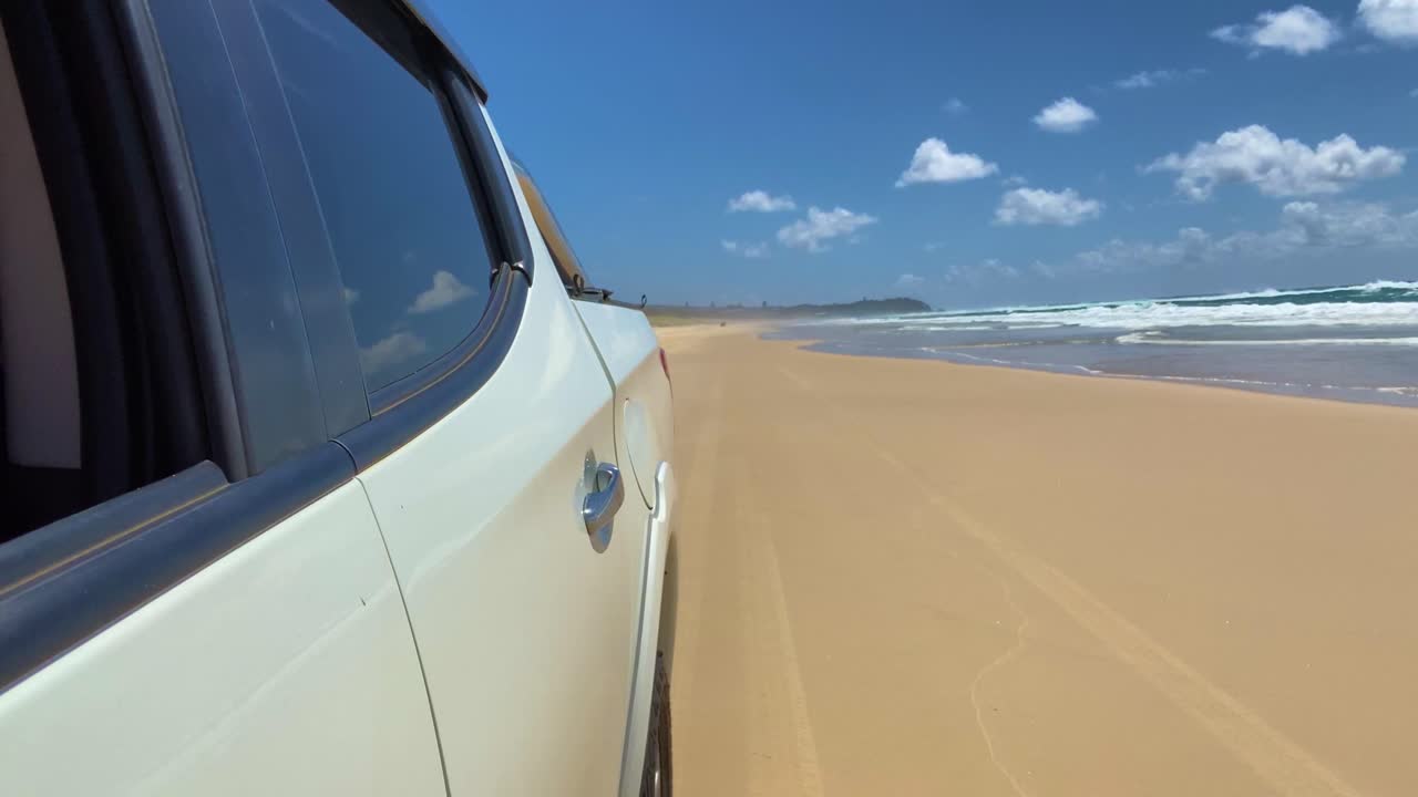 Fast travelling POV shot looking backwards along a car, back down the quiet beach towards Point Lookout on North Stradbroke Island
