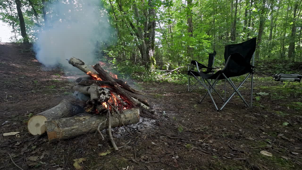 куча леса на огне в открытом районе, окруженном деревьями с креслом для кемпинга