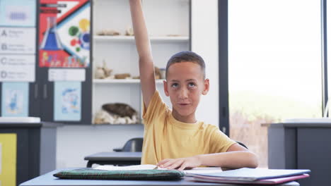 biracial boy in a classroom raises his hand, eager to answer a question in school