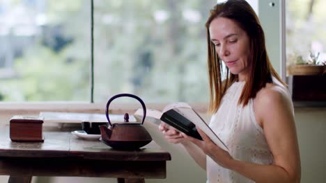 Attractive-middle-age-Hispanic-woman-reading-a-book-in-the-kitchen-nook-with-a-cup-of-tea