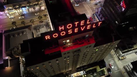 Establishing-view-of-famous-The-Hollywood-Roosevelt-Hotel,-aerial-flyover-at-night-looking-down-onto-the-streets-in-Los-Angeles