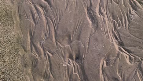 Patterns-in-the-sand-made-from-rippling-water,-waves,-and-seagulls-4K-30FPS-Slow-Motion