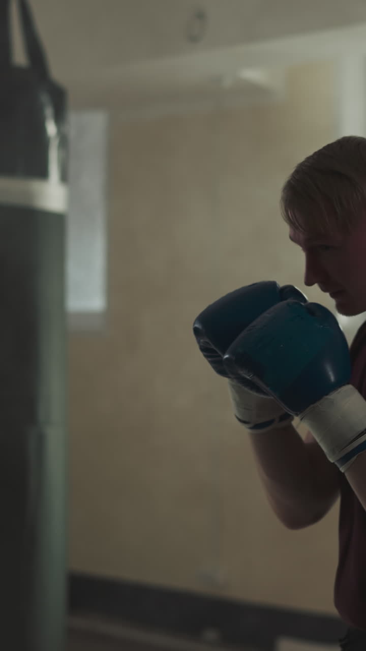 un boxeador lucha con una bolsa de boxeo en un gimnasio vacío. un hombre fuerte con guantes de boxes golpea a una bolsa colgada en un club de lucha en cámara lenta. un maestro de artes marciales