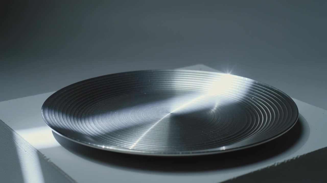 Sweeping beam moving across metallic dish with concentric ridges on plinth, creating star flare