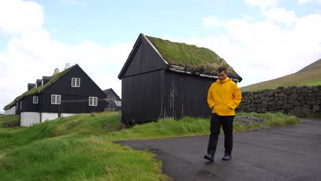 Man-in-yellow-raincoat-walks-near-traditional-Faroese-houses-of-Vidareidi,-Vidoy-Island