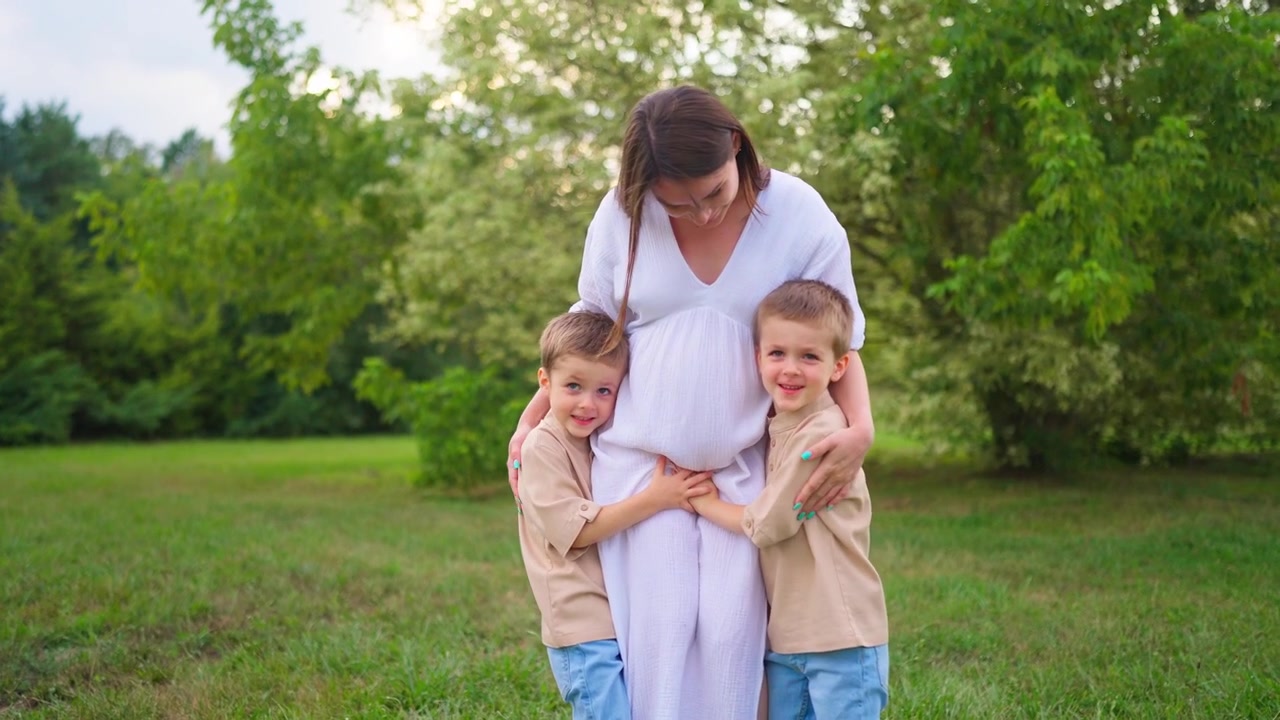 Mãe Grávida Feliz Abraçada por Seus Dois Filhos Pequenos no Parque