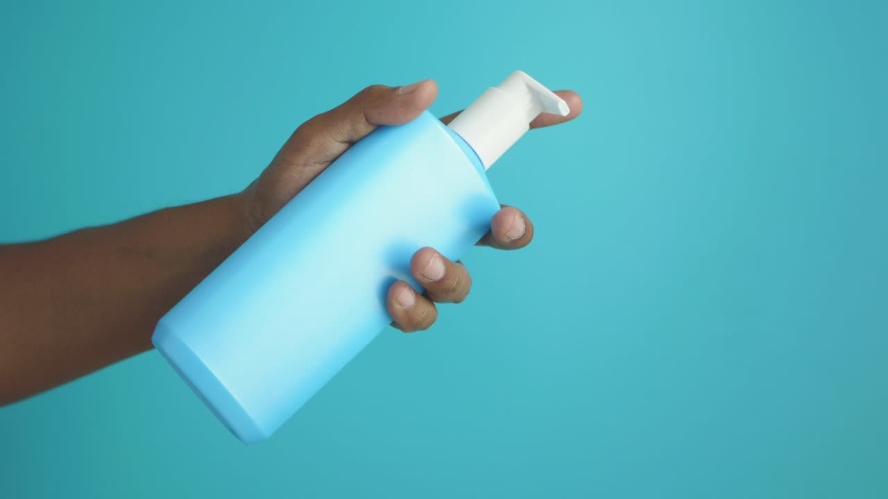 close-up de uma mão segurando uma garrafa de bomba azul de desinfetante para mãos
