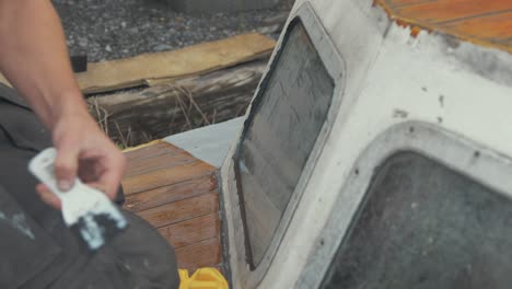 young carpenter flattening sika flex mastic sealant on windows on bow of wooden boat