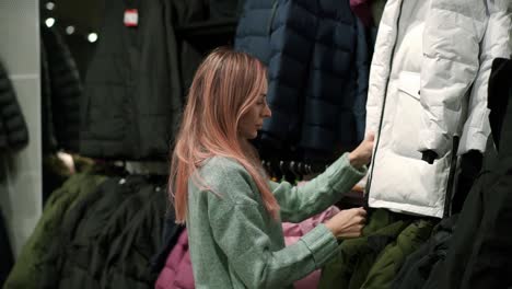 woman is taking a new down jacket from a rack to fit it