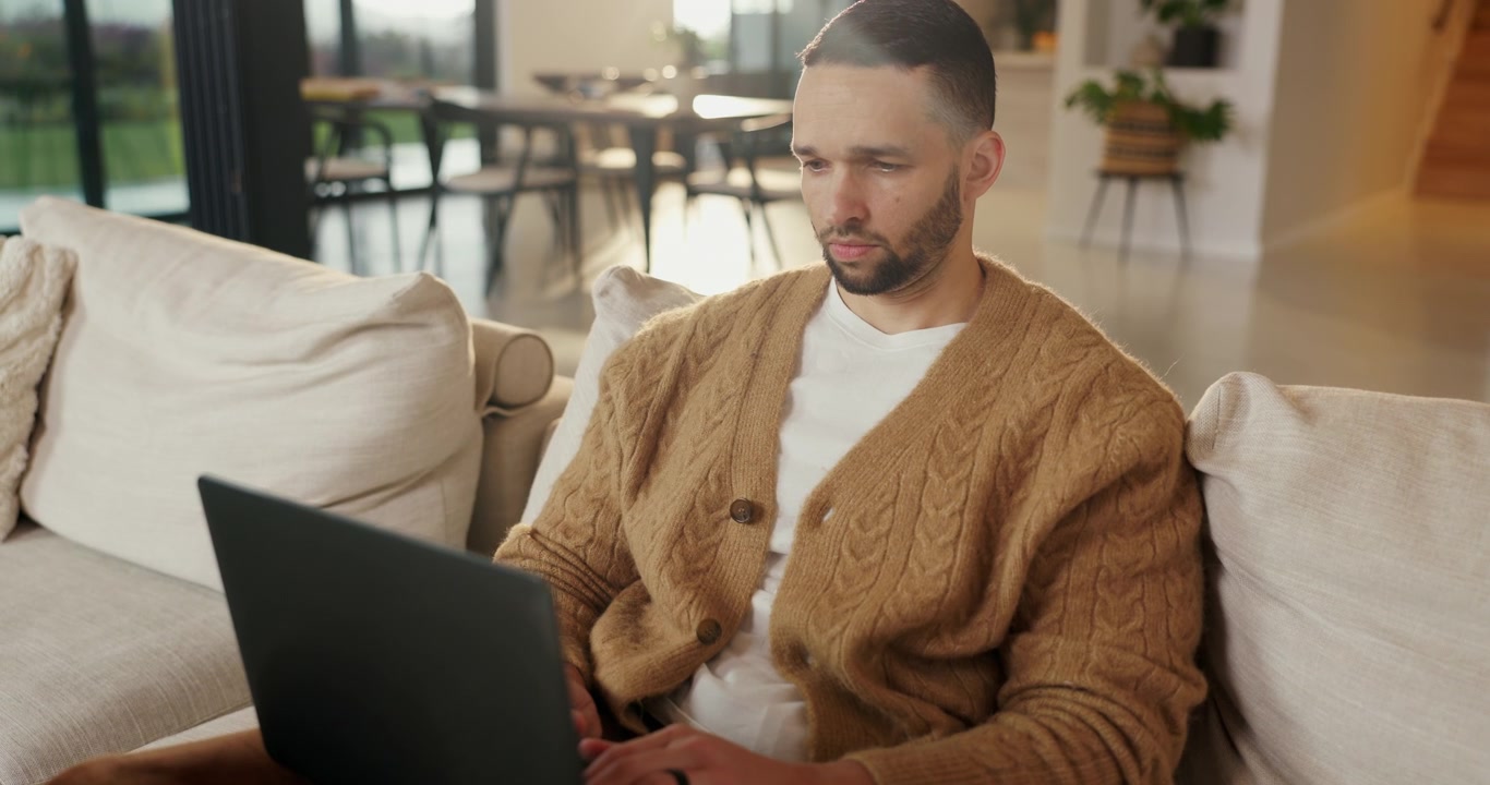 Focused Man Working on Laptop While Sitting on Sofa at Home