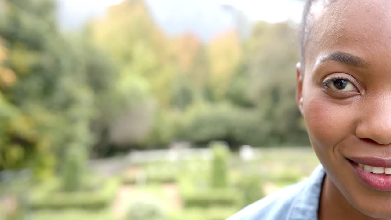 Portrait of african american woman looking at camera and smiling in garden, copy space, slow motion