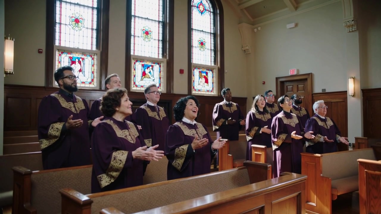 Singing choir raising hands clapping while song starting in church worship with stained glass robes