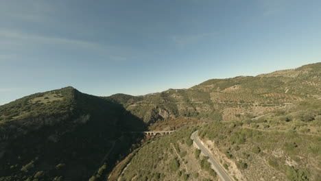 Aerial-view-of-arid-olive-grove-hills-and-old-arch-bridge-in-Spain