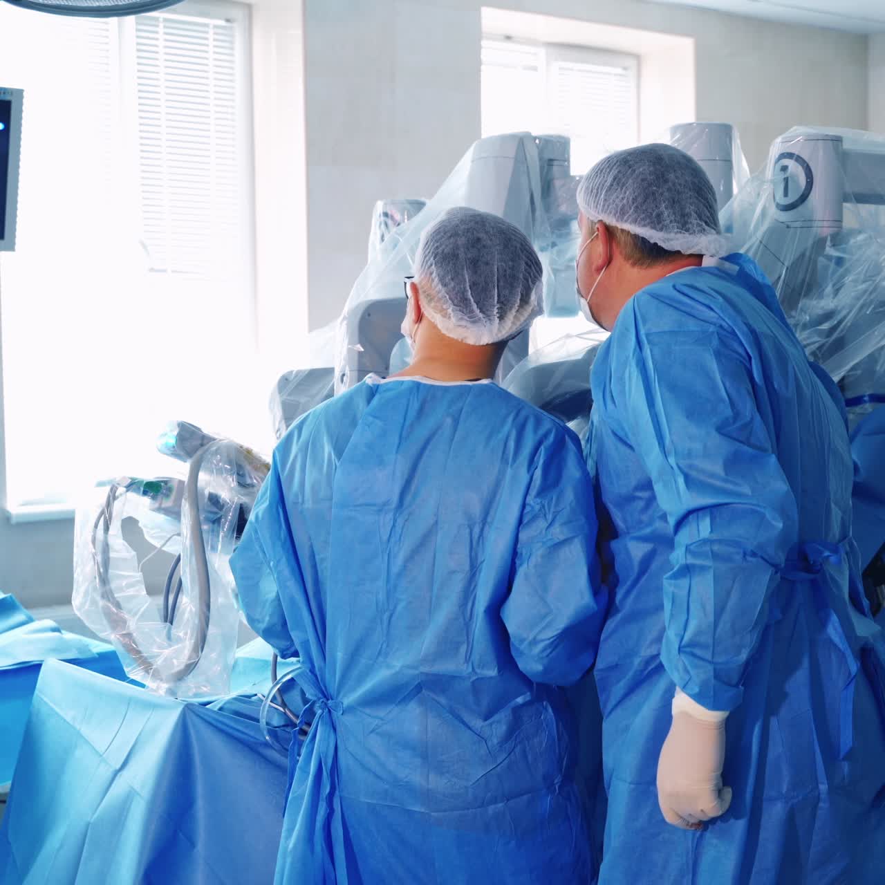 Operation with futuristic equipment. Backside view of two doctors looking on the screen with operating process. Robot in surgery.