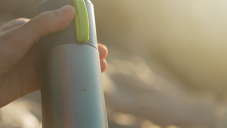 man closes thermos as morning sun casts beautiful light on his hands during golden hour