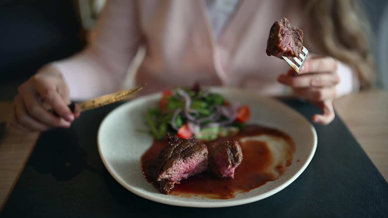 Close up of woman cutting juicy grilled steak served with rich sauce and fresh salad