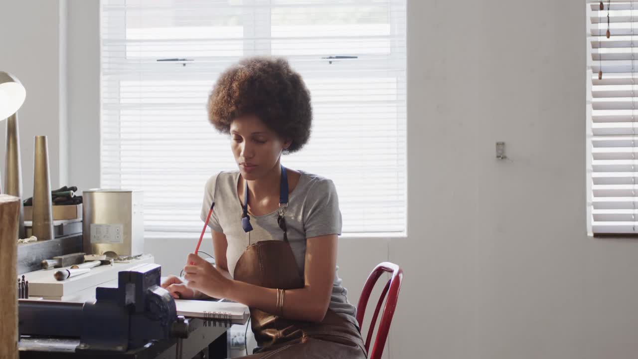 Busy biracial female worker doing design of jewellery in workshop in slow motion