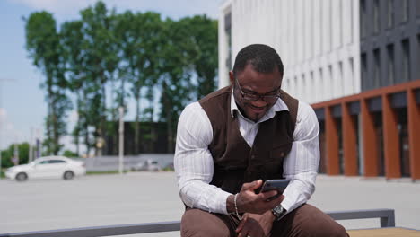 portrait of positive african american man mixed race. afro guy freelance businessman user talking by mobile phone. black man answering call sitting outdoors in city.