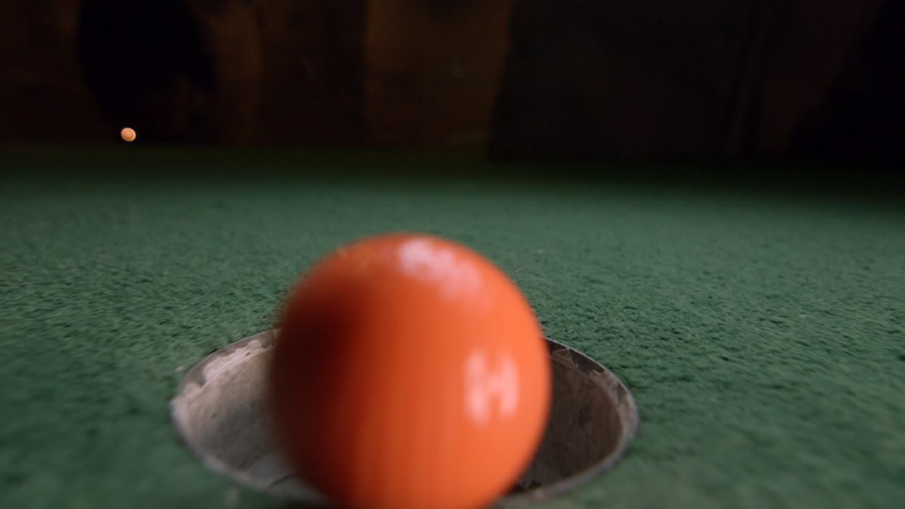 오렌지색 미니 골프공이 골프 홀에 떨어지고 코스의 주머니에 튕긴다