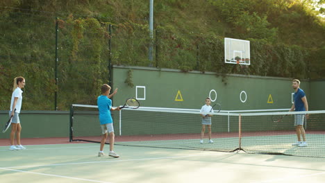 happy family playing tennis on an outdoor court in summer 2