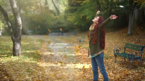 4k slow motion: beautiful young redhead woman standing in a park in autumn with leaves falling down around her