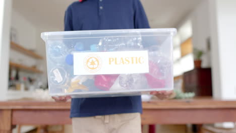 Midsection-of-african-american-boy-holding-recycling-box-in-kitchen,-slow-motion