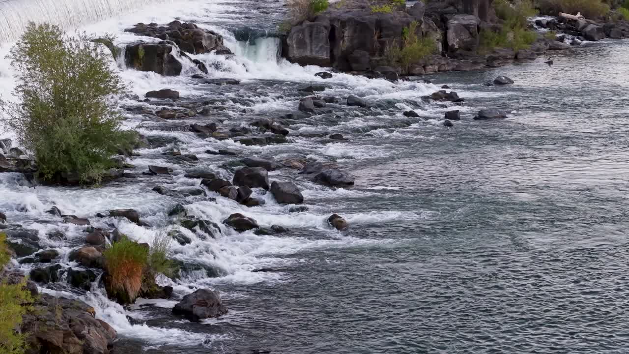 An aerial view of a rocky river where rushing water tumbles over stones, creating small rapids and swirling currents Idaho Falls