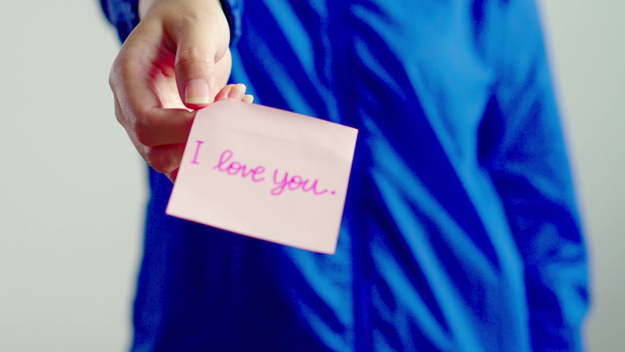 Close-up of hand offering pink "I love you" note for Valentine's or romantic themes