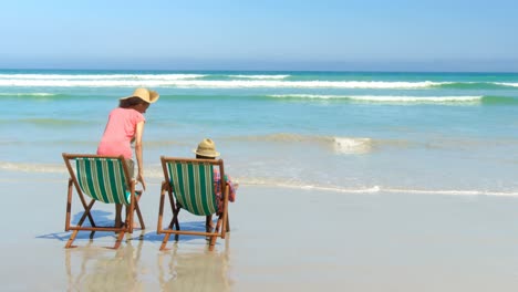vista trasera de una pareja afroamericana activa con sombrero relajándose en una silla de sol en la playa 4k