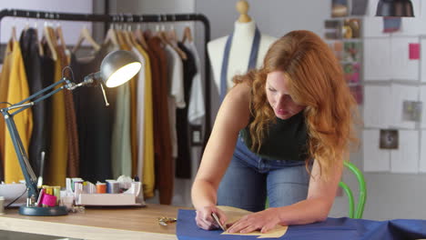 portrait of female clothes designer working in fashion studio drawing pattern on fabric in chalk